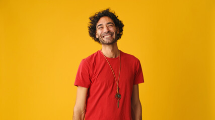 Smiling attractive man with curly hair, dressed in red T-shirt,  crossing his arms and looking at...