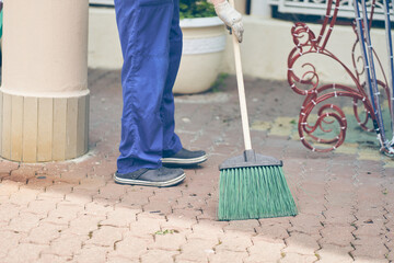 A janitor with a broom sweeps the paving slabs next to the building. A man in a work uniform is working on the street. High quality photo