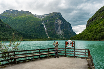 Asian woman traveler at the lake shore in mountains of Norway. Young female making video on...