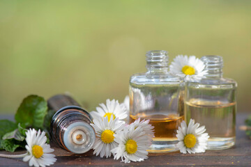 bottles of essential oil and daisies with fresh mint leaf on a wooden table  outdoors - 793728773
