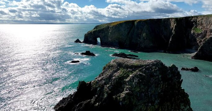 Drone flying over seastack with birds nesting to headland with sea cave emerald green seas and dramatic sky Copper Coast in Waterford Ireland