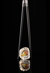 a close-up shot of an uramacki  sushi roll being held up by chopsticks against a black background...