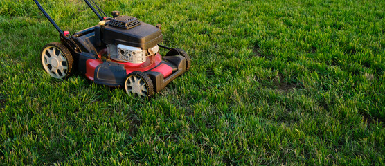 Obraz na płótnie Canvas Lawn mower on green grass background. Petrol machine for cutting. Garden care. Electric equipment. Side view. Copy space. Lots of clover weeds. Sport lawn for games. Weed control. High quality photo