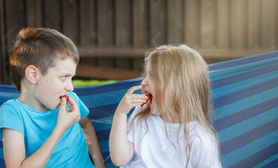 brother and sister eating Strawberry sitting in the blue hammock