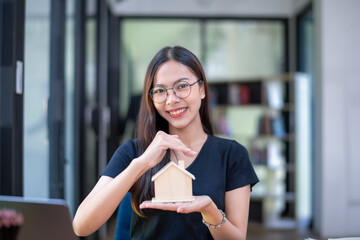 Smiling woman displaying a model house and a fan of cash, representing successful investment or...