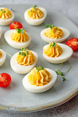 Deviled eggs with cheese, mustard and microgreens on top on a plate for Easter.