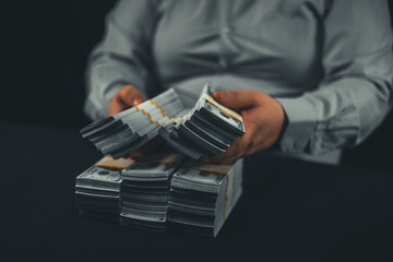 A businessman holds out bundles of dollars in his hands to the camera on a black background. A lot...