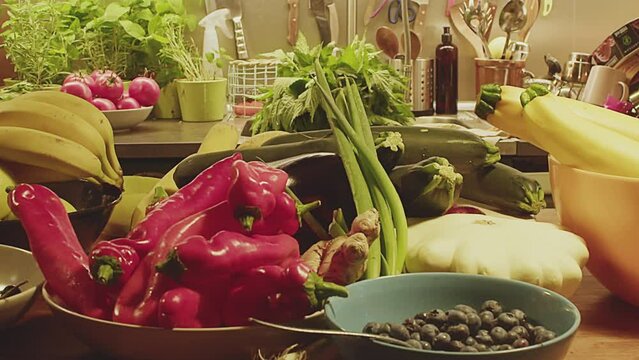 Slow motion close up of various whole fruits, herbs and vegetables on a kitchen table. Ball peppers, blueberries, ginger, summer squash, parsley and zucchini. Kitchen interior. Mixed vegetables