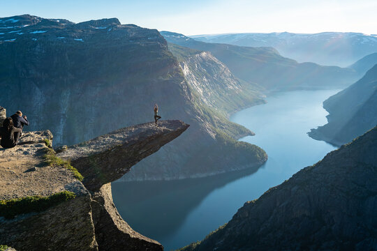 Trolltunga, Norway. Woman tourist doing yoga on the top of mountain's cliff edge named Trolltunga raising her hands up and watching amazing mountains view. Adventure travel sport healthy lifestyle.