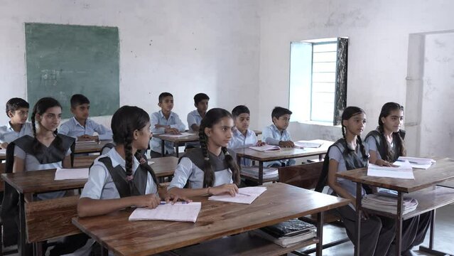 Rural Indian school students raise hands and answer to question of teacher in classroom. Elementary boys and girls studying, test or exams, Education in india concept.
