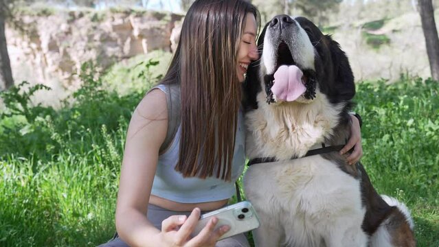 Woman taking selfie with happy dog in park. Young woman enjoys taking a selfie with her adorable dog amidst lush greenery and sunshine