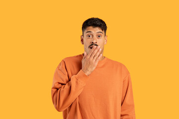 Surprised Young Man in Orange Sweater With Hand Over Mouth