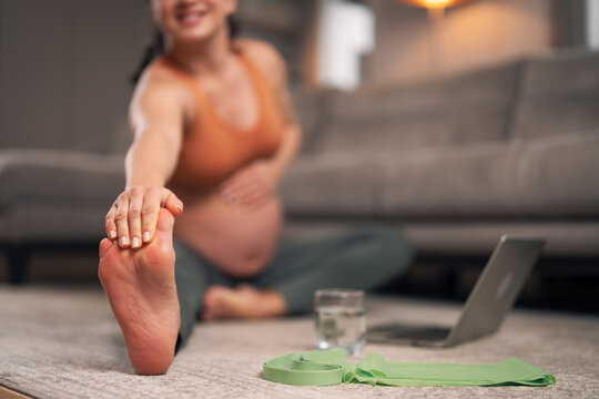 A close-up shot of a pregnant woman holding onto her toes and stretching
