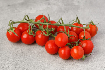 Branch of fresh red cherry tomatoes close up on textured stone table