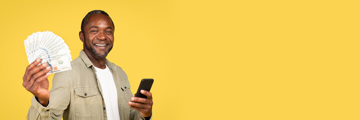 Glad mature black guy showing many dollars cash, using smartphone