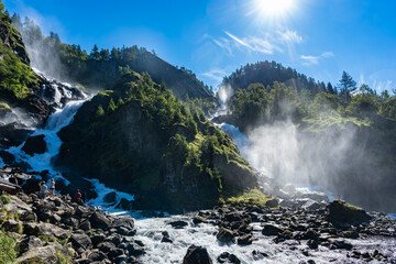 Beautiful high waterfall in Norwegian mountains. Lots of tourists watching enjoying falling water...