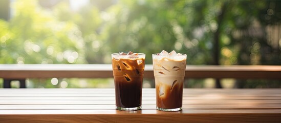 Two iced coffees on wooden table with green backdrop