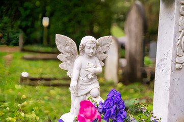 kleiner schöner Engel kniet hinter Blumen auf dem Highgate Cemetery in London Camden