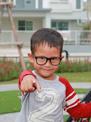 Portrait of Asian little boy child pointing straight at you and wearing glasses while stay in the garden. - 793793197