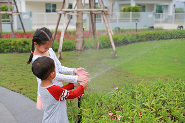 Asian little boy and young girl child having fun to play water of watering the plants. - 793793357