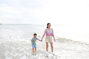 Happy Asian mom and son enjoy playing on tropical sand beach at sunrise. Happy family in summer holiday. - 793793901