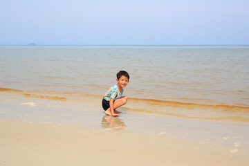 Portrait of Asian little boy child having fun and sitting on tropical sand beach with looking at camera. - 793794327