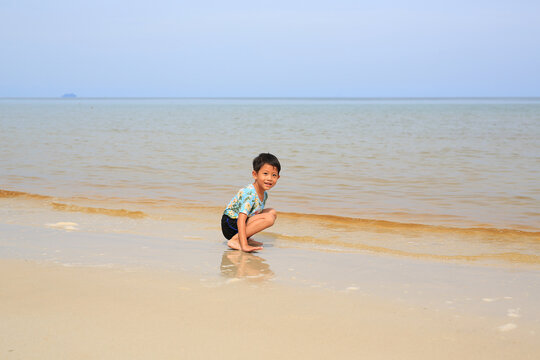 Portrait of Asian little boy child having fun and sitting on tropical sand beach with looking at camera.
