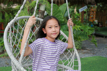 Close-up portrait of happy Asian girl child while play on the white cradle or swing in the garden. - 793794782