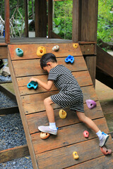 Asian little boy age about 5-6 years old trying climb on wooden board equipment at playground. - 793795107