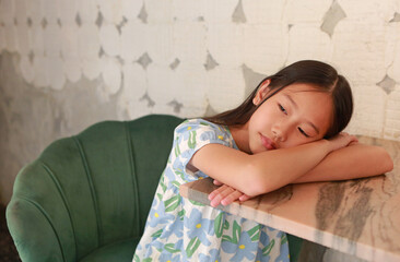 Portrait of Asian girl kid age about 9 years old sit on sofa chair and lying on marble table with looking beside.