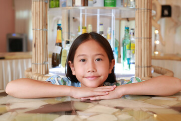 Portrait closeup of happy Asian girl kid sit on chair and lying at marble table with looking camera. - 793795360