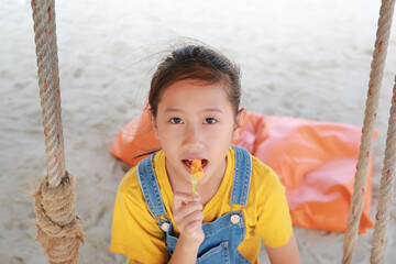 Close up of Asian girl eating French fries with dip cheese while sitting on swing at the beach. - 793796773