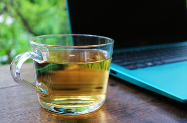 Closeup of a glass of hot tea with an opened laptop