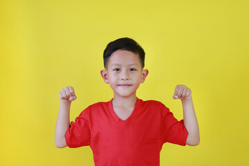 Smiling Asian little boy showing his muscle with looking camera isolated on yellow background. Kid show strong gesture. - 793797548