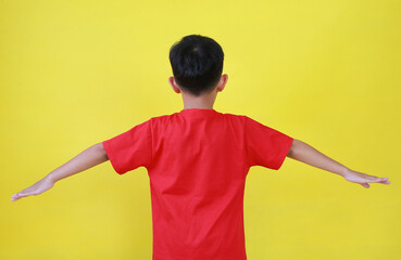 Back view of Asian boy child open hands outstretched. Kid standing and spread his arms wide isolated on yellow background. - 793797963