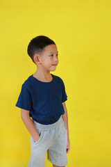 Smiling Asian little boy child put hand in his pocket of pants and looking beside over yellow studio background.