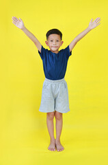 Asian boy child raised hands up. Kid standing and raise arms isolated on yellow background. Image full length. - 793798159