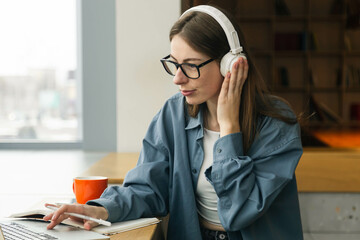 Portrait of smiling woman sitting at desk, using laptop and writing in notebook.