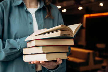Young woman with a pile of books on a blurred library background.