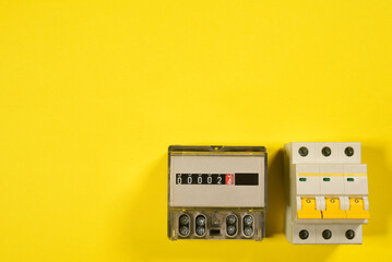 Electricity meter and automatic switch circuit breaker close up on the yellow flat lay background.
