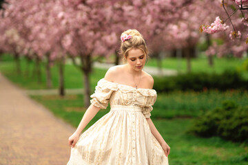 Pretty young blonde girl  in vintage lace dress  standing in spring park near pink blossom flowers....