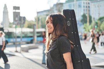 portrait of a young music student walking with guitar case on her back