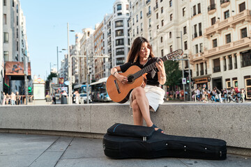 young music student sitting in the city playing the acoustic guitar. full view of latin woman with...