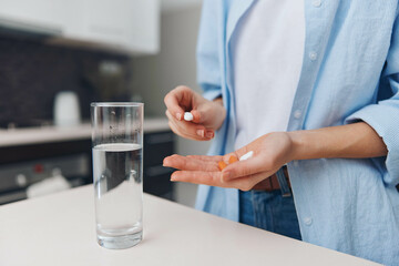 Female taking medication with a glass of water and pill bottle on a table in a modern interior setting