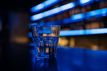 A glass of water sits on a bar counter. The bar is dimly lit, giving the scene a cozy and intimate atmosphere.