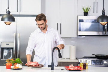 Handsome man cooking in kitchen. Mature man cooking with vegetables and meat in kitchen interior. Caucasian man cook tasty lunch in kitchen. Guy prepare healthy food for dinner in kitchen.