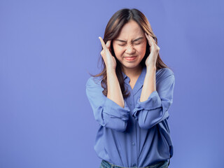 An Asian woman in a blue shirt and jeans covers her ears and screams with an angry expression against a solid blue background