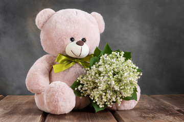 A pink teddy bear is holding a bouquet of white flowers lilies of the valley