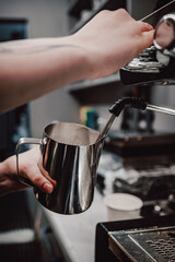 Barista skillfully steaming milk in a stainless steel pitcher with an espresso machine,...