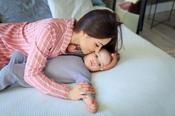 Young happy mother and baby lying on bed together, smiling, kissing and playing. Mommy looking at...